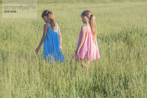 Ein junges Mädchen folgt seiner Schwester und geht durch ein sonniges Feld.