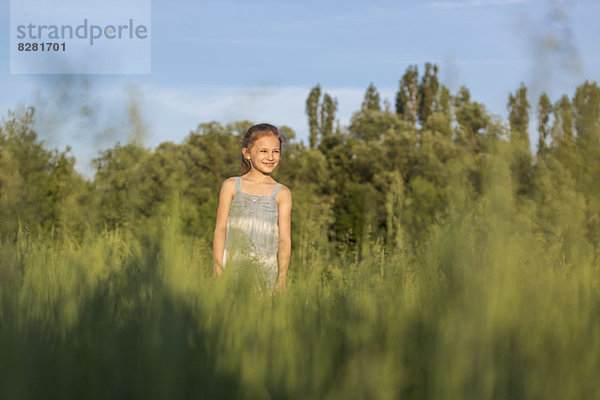 Ein junges  fröhliches Mädchen steht auf einem Feld und schaut auf die Aussicht.