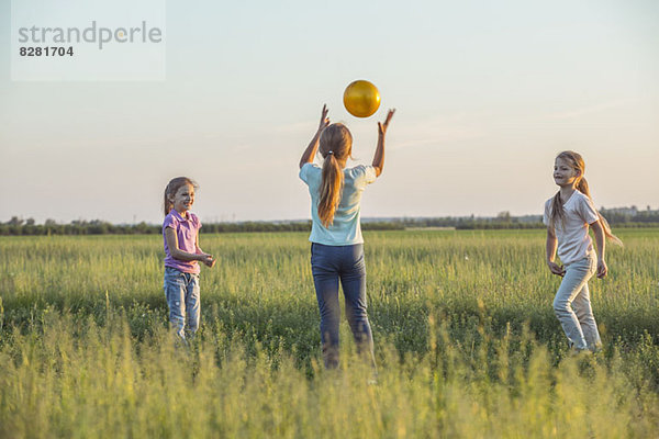 Drei junge Mädchen beim Fangen auf einem sonnigen Feld im Sommer