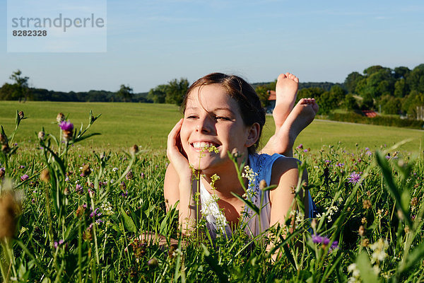 Lächelndes Mädchen liegt in einer Blumenwiese