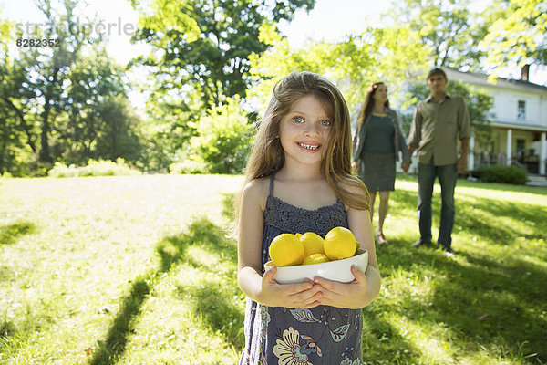 Bauernhof. Kinder und Erwachsene arbeiten zusammen. Ein Mädchen hält eine Kiste mit Zitronen und frischen Früchten. Zwei Erwachsene im Hintergrund.