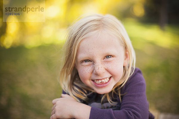 Ein Mädchen sitzt im Gras und lächelt mit einem strahlenden Lächeln. Nahaufnahme.