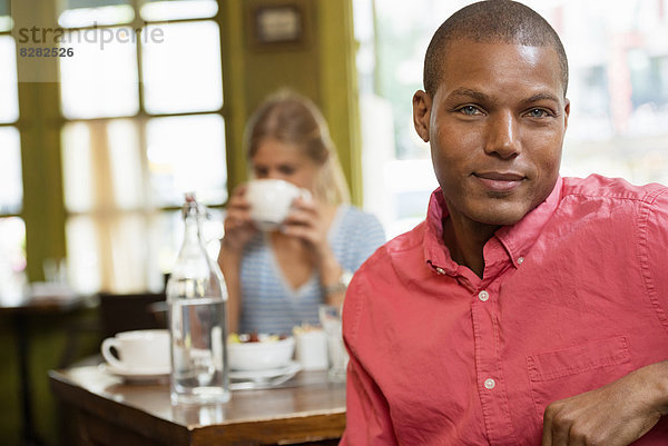 Ein Ehepaar in einem städtischen Kaffeehaus. An einem Tisch sitzen. Eine Frau hält eine Tasse Kaffee in der Hand.