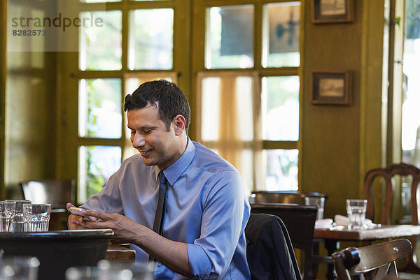 Geschäftsleute. Ein Latino-Mann  der allein an einem Tisch sitzt und seine Nachrichten abruft.