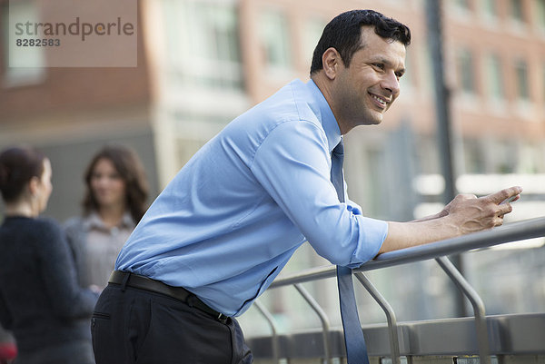 Geschäftsleute im Freien. Ein lateinamerikanischer Geschäftsmann in Hemd und Krawatte  angelehnt an einem Geländer. Entspannend.