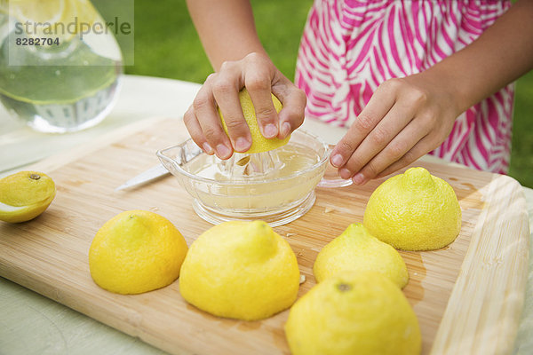 Eine Sommer-Familienzusammenkunft auf einem Bauernhof. Ein Mädchen schneidet Zitronen in Scheiben und entsaftet sie zu Limonade.