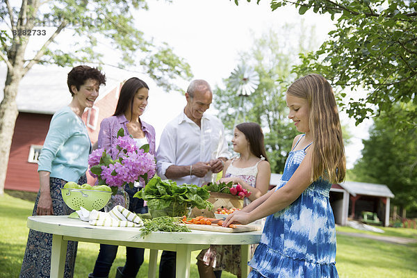 Familienfeier. Fünf Personen versammelten sich um einen Tisch und bereiteten frische Salate und Obst für eine Party vor. Zwei Mädchen  eine junge Frau und ein reifes Ehepaar.
