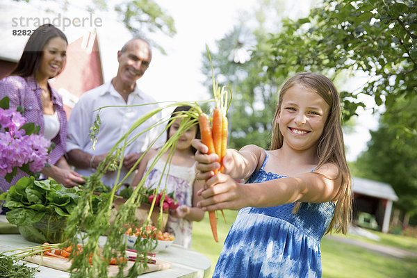 Familienfeier. Ein gedeckter Tisch mit Salaten und frischem Obst und Gemüse. Eltern und Kinder. Ein Kind mit frisch gepflückten Karotten.