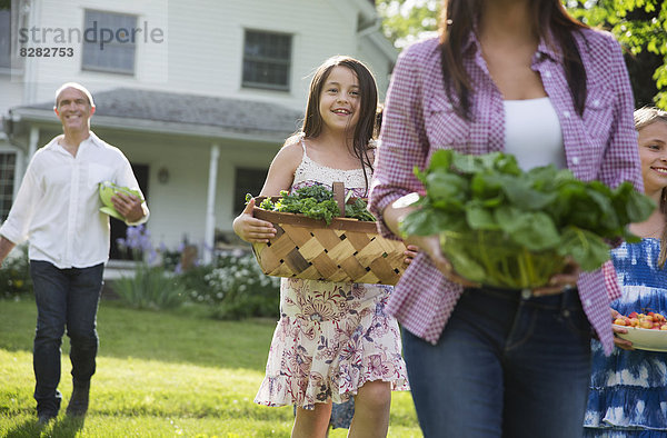 Familienfeier. Eltern und Kinder  die mit Blumen  frisch gepflücktem Gemüse und Obst über den Rasen laufen. Vorbereitungen für eine Party.