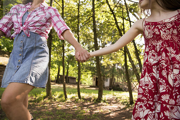 Eine Frau und ein junges Mädchen halten sich an den Händen und laufen unter den Bäumen entlang.