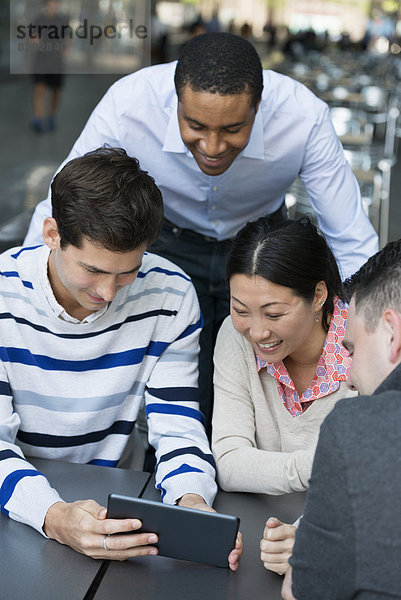 Geschäftsleute in Bewegung. Vier Personen haben sich zu einer Diskussion um ein digitales Tablet versammelt. Ansicht von oben.