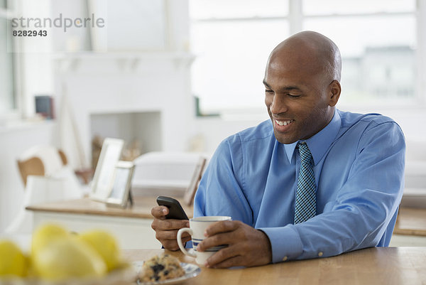 Ein Mann in einem blauen Hemd  der mit einem Smartphone an einer Frühstücksbar sitzt.