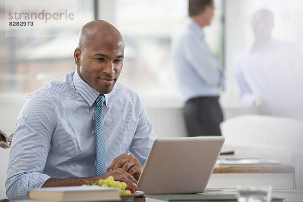 Büroleben. Ein Geschäftsmann in Hemd und Krawatte  der an einem Schreibtisch sitzt und einen Laptop-Computer benutzt.