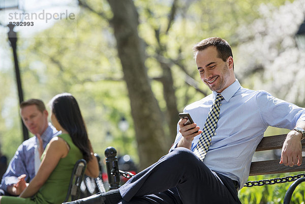 Ein Ehepaar auf einer Bank im Hintergrund  und ein Mann  der sein Telefon überprüft.