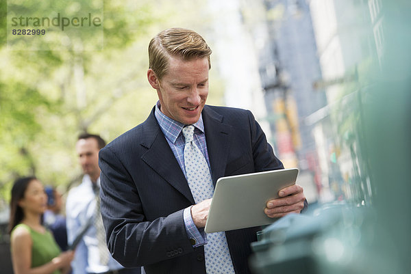 Drei Geschäftsleute im Freien in der Stadt. Ein Mann mit einem digitalen Tablet  und ein Paar im Hintergrund.