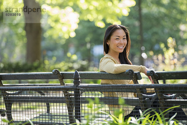 Eine Frau sitzt in einem Stadtpark auf einer Bank im Sonnenschein.