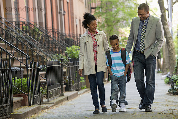 Eine Familie im Freien in der Stadt. Zwei Eltern und ein junger Junge gehen zusammen spazieren.