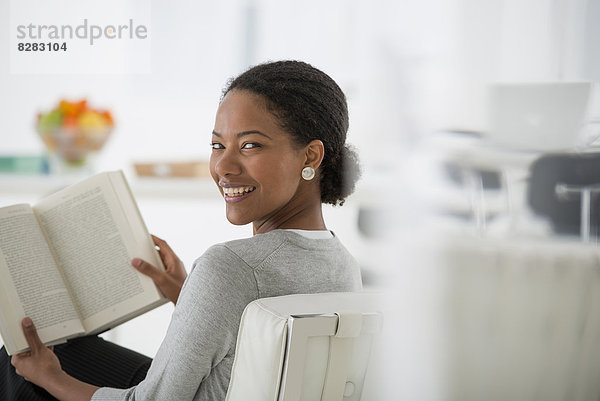 Wirtschaft. Eine Frau  die sitzt und ein Buch liest. Forschung oder Entspannung. Über die Schulter schauend und lächelnd.