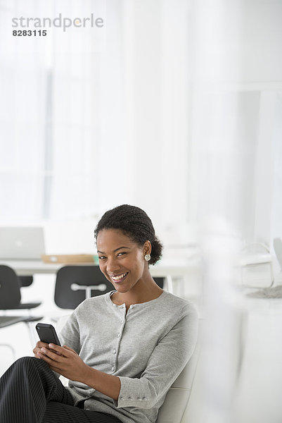 Wirtschaft. Eine Frau  die in einem bequemen Stuhl sitzt und ihr Smartphone auf Nachrichten überprüft.