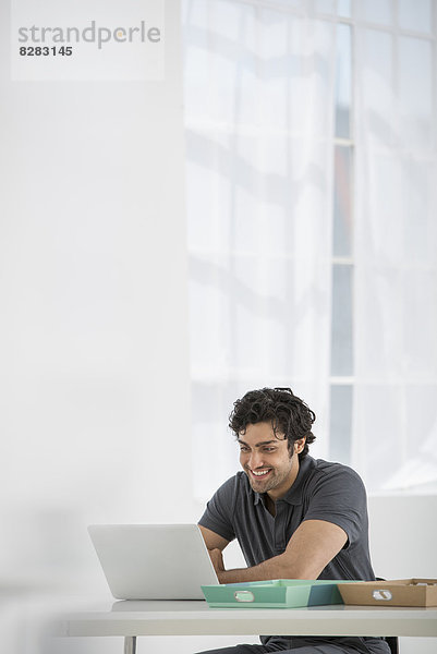 Ein Mann sitzt mit einem Laptop an einem Schreibtisch.