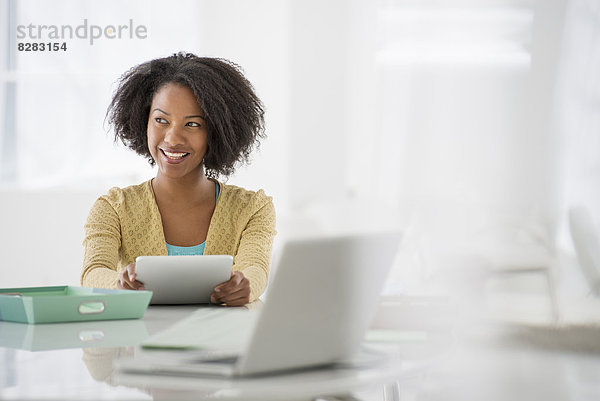 Wirtschaft. Eine Frau sitzt an einem Schreibtisch. Digitales Tablet und Laptop  und grüne Akten.