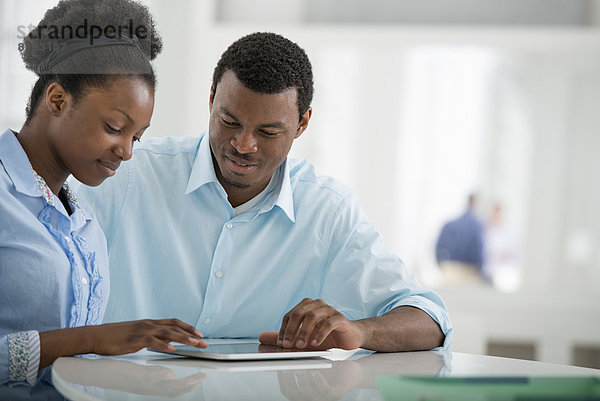 Innenministerium. Ein Mann und eine Frau  die Seite an Seite sitzen und ein digitales Tablet benutzen.