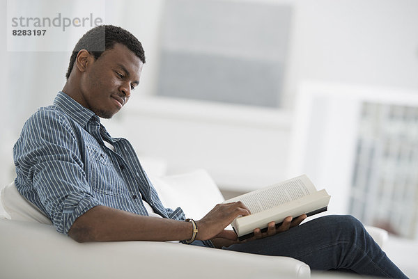 Ein strahlend weißer Raum im Inneren. Ein Mann sitzt und liest ein Buch.