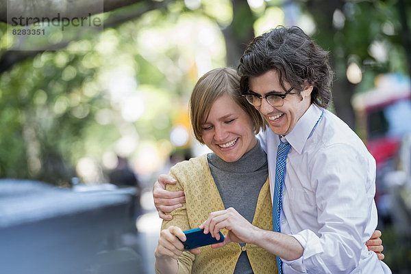 Stadt. Zwei Menschen  ein Mann und eine Frau im Freien  die sich gemeinsam ein Smartphone anschauen.