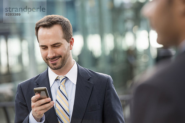 Stadt. Ein Mann im Geschäftsanzug  der seine Nachrichten auf seinem Smartphone abruft.