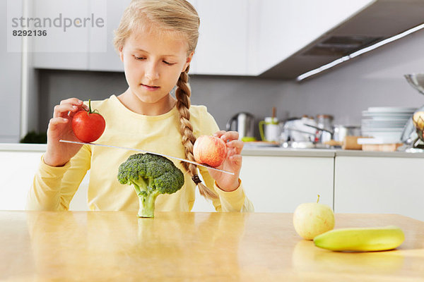 Mädchen balanciert Äpfel auf Brokkoli Schuppen