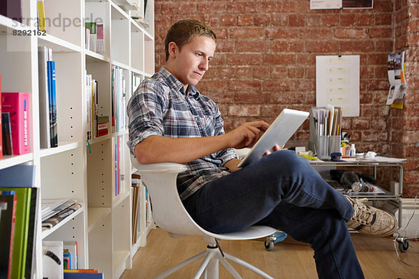 Junger Mann auf Stuhl sitzend mit digitalem Tablett