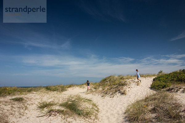 Bruder und Schwester laufen über Sanddünen.