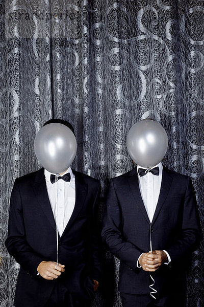 Porträt zweier junger Männer mit Luftballons vor den Gesichtern