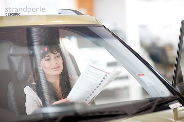 Mittlere erwachsene Frau liest Auto-Broschüre im Showroom