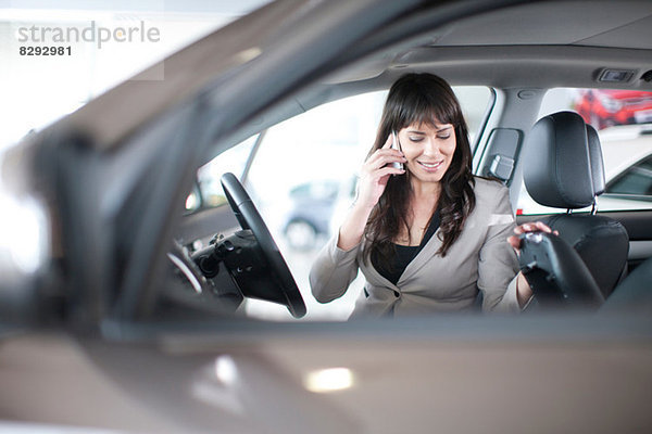 Mittlere erwachsene Frau mit Handy im Autohaus
