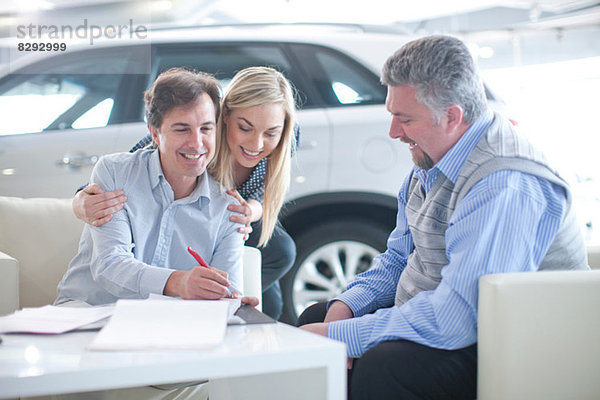 Autoverkäufer und Pärchen unterzeichnen Vertrag im Autohaus