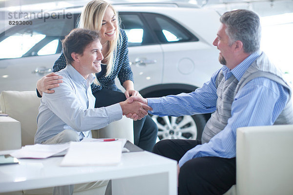 Autoverkäufer und Ehepaar beim Händeschütteln im Autohaus
