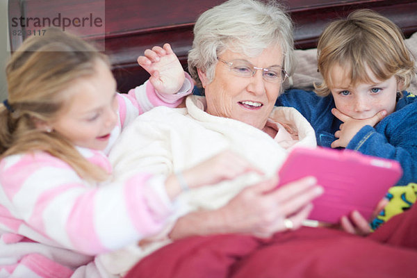 Großmutter und Enkelkinder spielen digitales Spiel im Bett