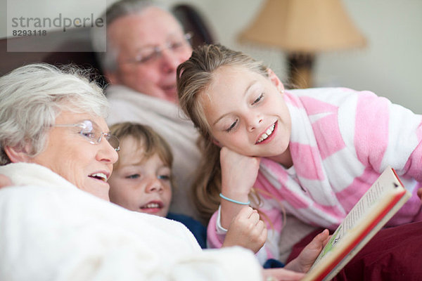 Großeltern und Enkelkinder lesen Märchenbuch im Bett