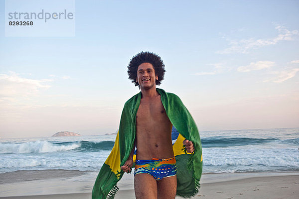 Junger Mann am Strand  in die brasilianische Flagge gehüllt