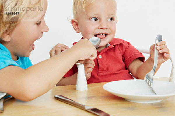 Zwei kleine Jungen bei Tisch  einer gibt vor  den anderen zu füttern.