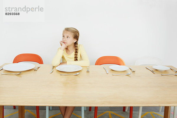 Mädchen am Tisch sitzend mit leerem Teller  wegschauend