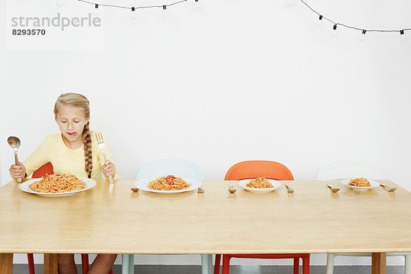 Mädchen am Tisch sitzend mit Spaghetti und drei weiteren Tellern