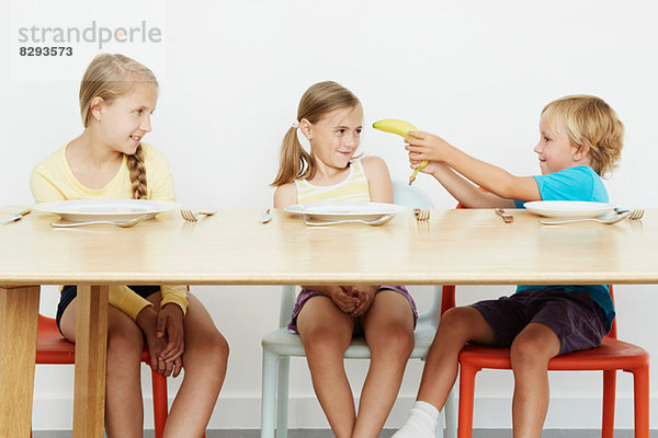 Drei Kinder am Tisch  Junge hält Banane
