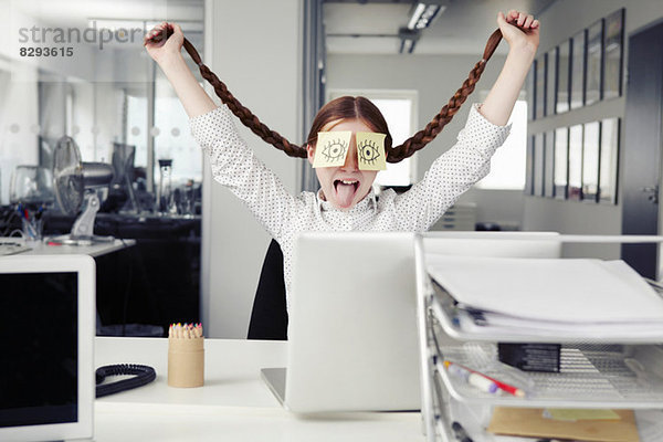 Mädchen im Büro mit Haftnotizen  die die Augen bedecken und Zöpfe halten.