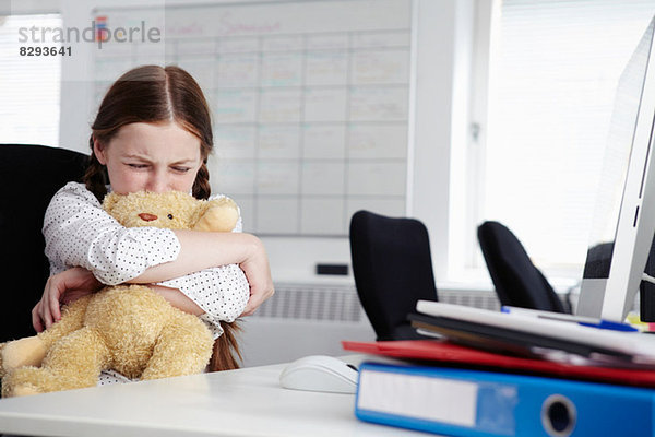 Mädchen im Büro sitzend  Teddybär umarmend und weinend