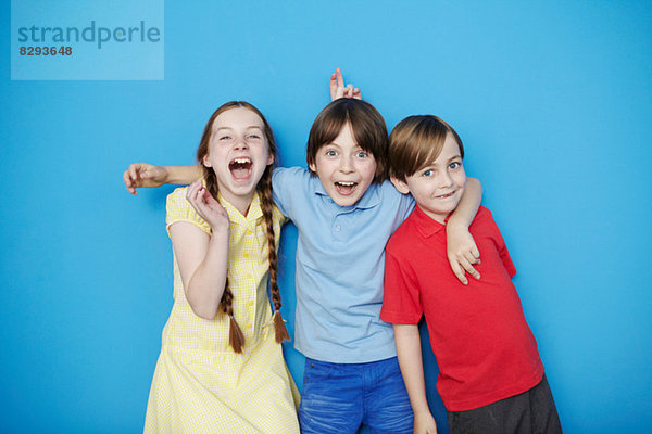 Porträt von drei Kindern mit Armen umeinander auf blauem Hintergrund