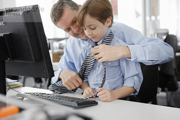 Vater legt Krawatte auf Sohn auf den Schreibtisch