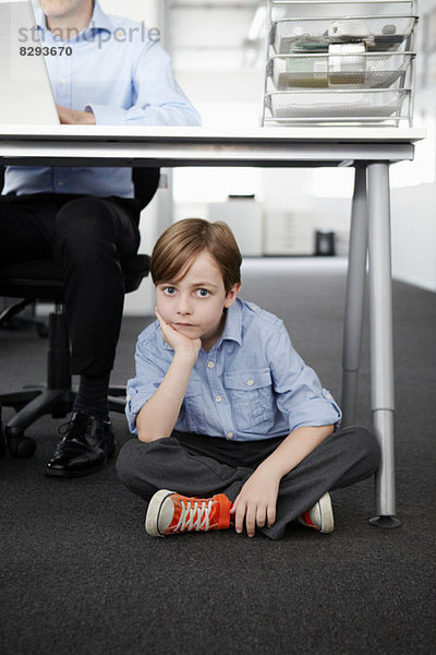 Junge auf dem Boden sitzend mit Geschäftsmann am Schreibtisch