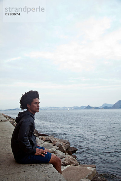 Junger Mann auf der Wand sitzend mit Blick aufs Meer  Rio de Janeiro  Brasilien